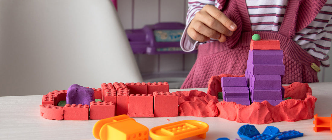Child playing with Mad Mattr Quantum Pack, using colorful molds and building soft, brick-shaped creations on a table.