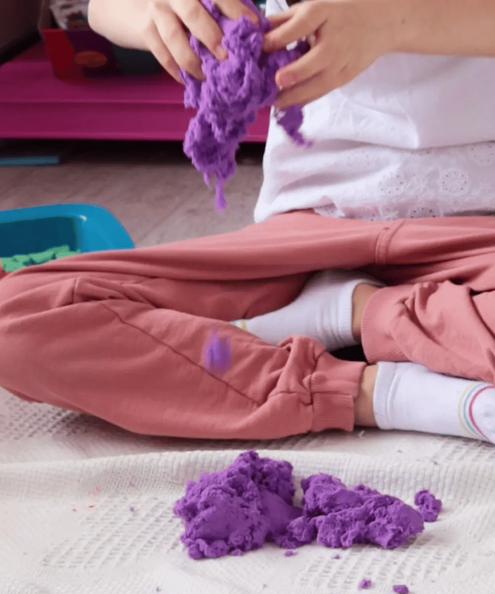 Mess-free play: A child molding purple Mad Mattr sensory dough that pulls apart easily without leaving residue on the white rug or clothes.